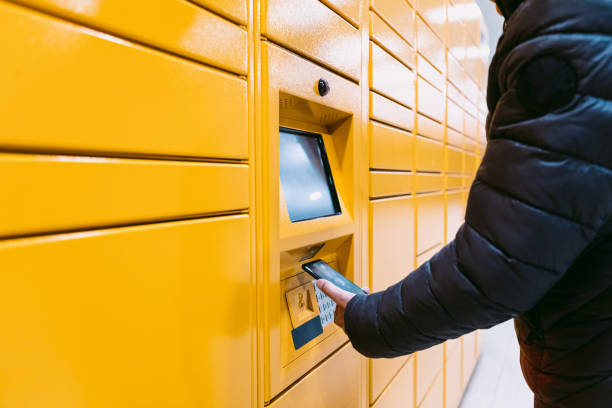 Detail of the arm of a man scanning a code on the mobile phone to pick up a package from the yellow locker. Messaging concept, compare online, e-commerce and packages stock photo