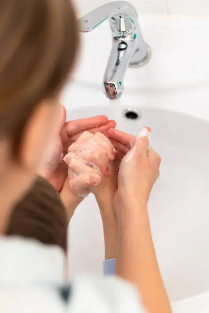 Photo of Mom helps the child wash his hands under running water from the faucet in the sink at home in the bathroom. Selective focus