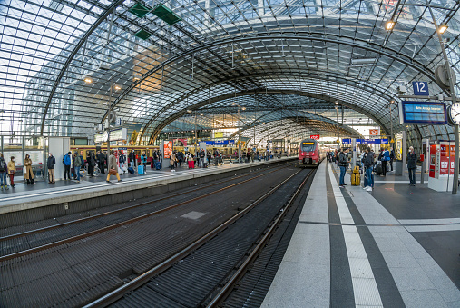 Berlin, Germany - August 21, 2021: The Berlin Hauptbahnhof is the main railway station located in Berlin, Germany. It was designed by the architect Meinhard von Gerkan of Gerkan, Marg and Partners. Passengers and tourists are waiting on the train station in the shot. Train moving into the station.
