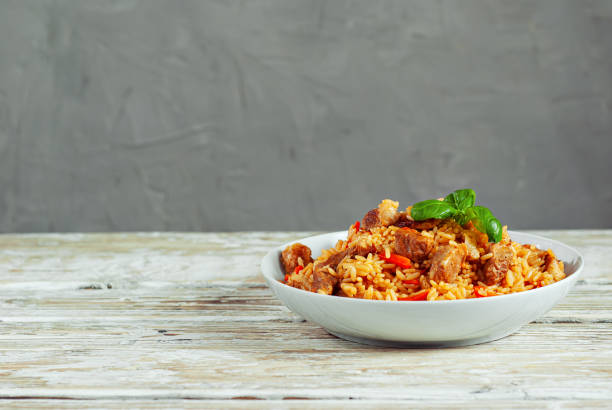 Pilaf in a white plate on a light background. Rice with basil on an old wooden board. Food on shabby wooden table. Copy space and war place for text near food. Pilaf in a white plate on a light background. Rice with basil on an old wooden board. Food on shabby wooden table. Copy space and war place for text near food. pilau rice stock pictures, royalty-free photos & images