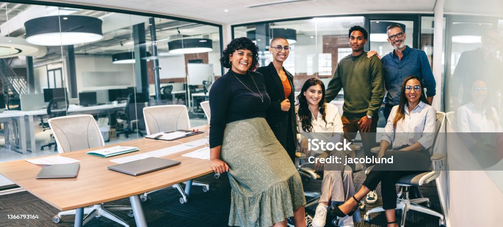 Team of businesspeople smiling at the camera in a boardroom Team of businesspeople smiling at the camera in a boardroom. Cheerful businesspeople grouped together in a modern workplace. Diverse team of businesspeople looking cheerful. Multiracial Group Stock Photo