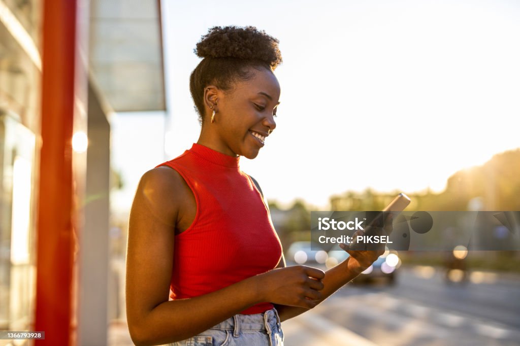 Young woman with smartphone waiting at the bus stop Using Phone Stock Photo