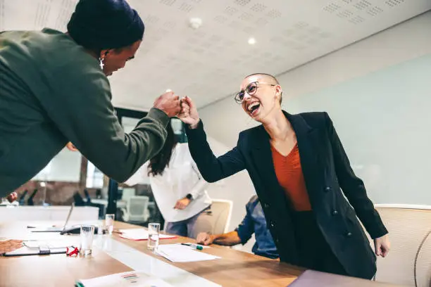 Young businesspeople fist bumping each other before a meeting in a boardroom. Two colleagues smiling cheerfully while greeting each other. Group of businesspeople attending a briefing in a modern office.