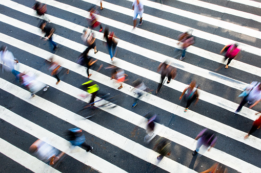 Group of unidentified people (motion blur) crossing a crosswalk that forms diagonal lines.