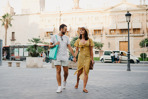 A girl and her boyfriend are walking holding each other's hand in Spain.
