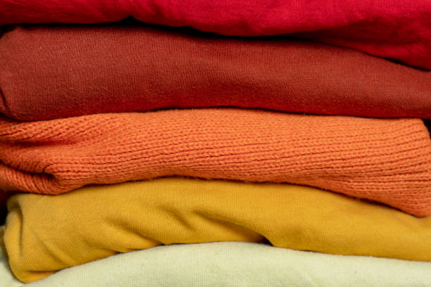 A stack of multi-colored fabric in warm colors. Background with folded clothes in red and yellow tones. T-shirts of different colors