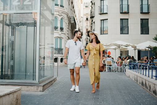 A girl in a hat and her boyfriend with a beard are walking through the old town.