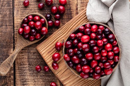 Ripe cranberry in wooden bowl on wooden table.