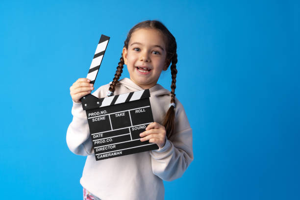 istock Smiling girl holding clapper board against blue background 1366799685