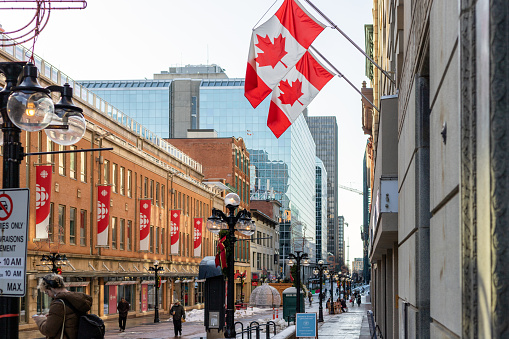 Ottawa, Canada - July 1, 2021: Cityscape with walking people and canadian flags on walls in downtown of Ottawa. Sparks street during winter holidays.