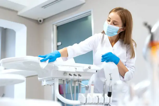 Side view of dentist assistant wiping modern dental equipment. Contemporary stomatology clinic service. Oral medicine sector. Safety and sanitary standards compliance