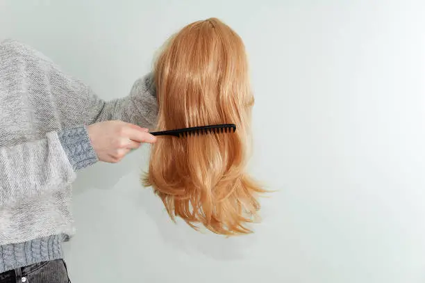Caucasian woman combing her red wig with a comb.