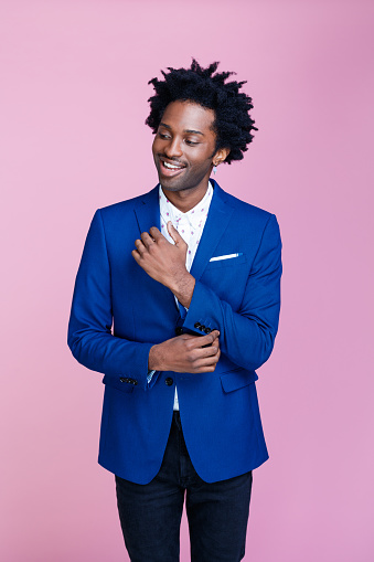 Friendly afro american man wearing navy blue suit jacket and white shirt, looking away and smiling. Studio shot on pink background. Portrait of designer.