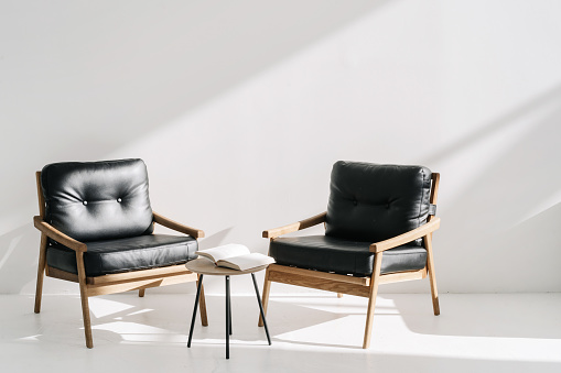 Two minimalistic leather armchairs standing near coffee table in luxury office or bright stylish apartment. Open book, agenda or planner in meeting room at business center