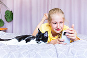 Girl with mobile phone and black and white cat lying next to each other on bed.
