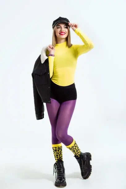 Fashion studio portrait of a beautiful girl in bright lemon golf, purple tights and neon leopard print socks.