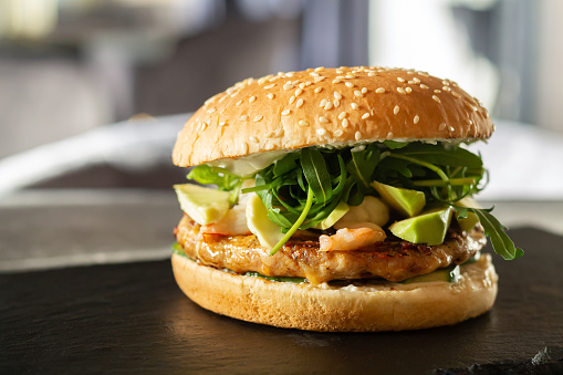 Juicy chicken burger with shrimps, avocado, cheese, sauce, lettuce and fresh sesame bun on fast food restaurant table