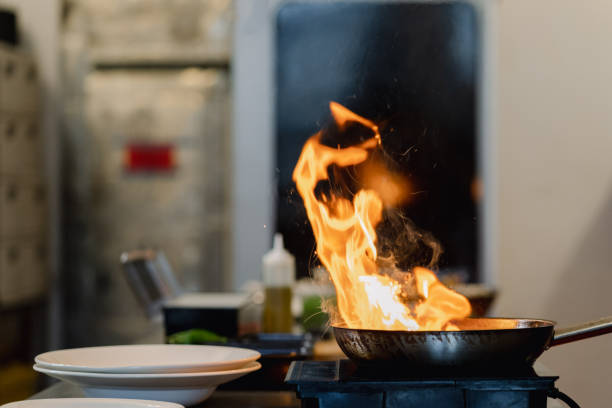 Chef cooking with flame in a frying pan on a kitchen stove