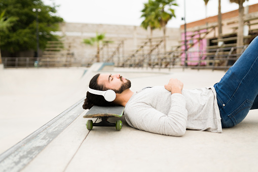 I'm so relaxed. Tired young man resting and lying on the floor of the skatepark. Attractive man relaxing with music and a skateboard