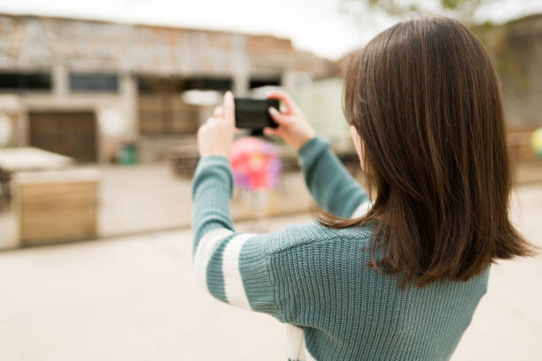 Rear view of a young woman taking a photo or short video outdoors to post on her social media platform