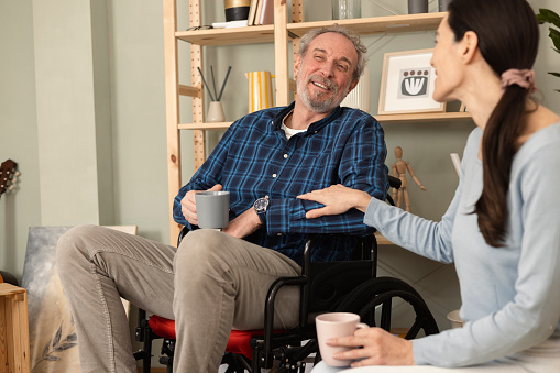 Mature man in a wheelchair enjoying coffee with his wife at home