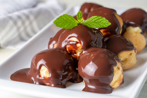 Delicious profiteroles with chocolate and white plate. Selective focus image on light background.