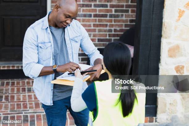 Female Delivery Driver Holds Tablet For Customer To Sign Stock Photo - Download Image Now