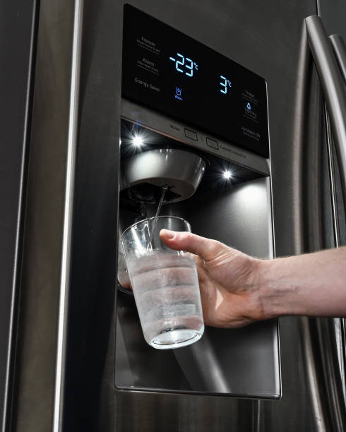 Home fridge dispenser filling glass held by hand at night stock photo