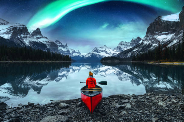 femme voyageuse assise sur un canot avec des aurores boréales au-dessus de l’île spirit dans le lac maligne au parc national jasper - aurore boréale photos et images de collection