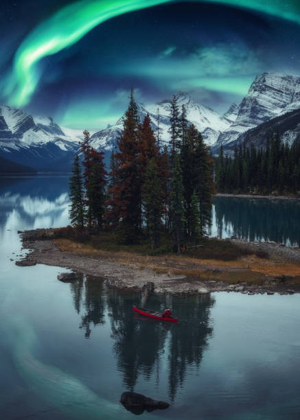 uomo viaggiatore in canoa su spirit island con aurora boreale sulle montagne rocciose nella notte al parco nazionale di jasper - lago maligne foto e immagini stock