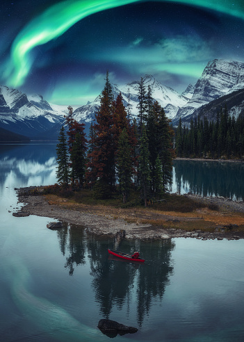 Traveler man canoeing on Spirit Island with aurora borealis over rocky mountains in the night at Jasper national park, Alberta, Canada