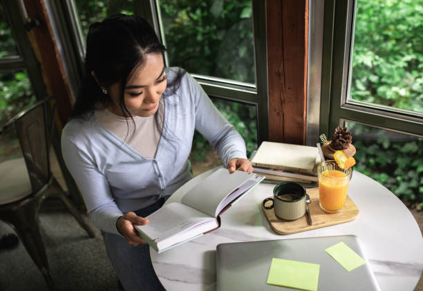 istock Young Asian woman sitting in cafe reading a book. 1366827521