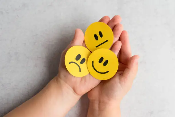 Kid’s hands holding happy, sad and unsatisfied paper faces.