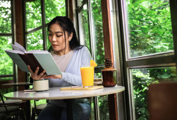 istock Young Asian woman sitting in cafe reading a book. 1366829687