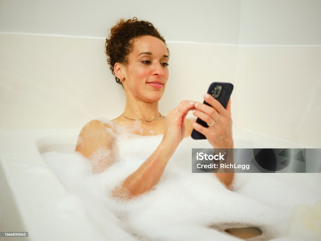 Woman Enjoying a Bubble Bath A woman relaxing in a bathtub full of bubbles. Mobile Phone Stock Photo