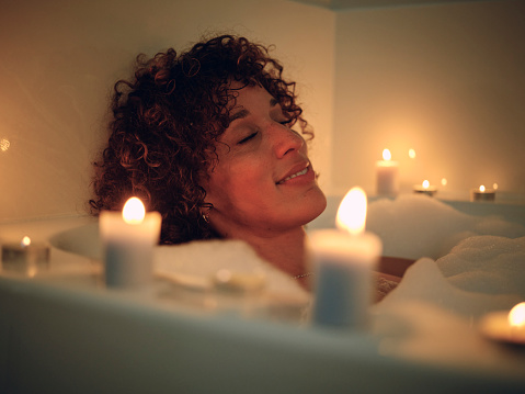 A woman relaxing in a bathtub, full of bubbles and surrounded by candles.