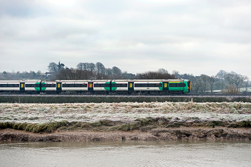 Southern Railway passenger train passes through winter landscape at Arundel, West Sussex, England. Arundel is an ancient market town built at a bridge point over the River Arun, with a skyline dominated by the huge Arundel Castle - built by the Normans - and the Gothic revival architecture of Arundel Cathedral which overlooks the meadows and grasses of the fertile South Downs