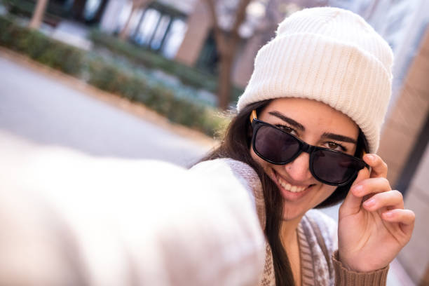 Young smiling girl with sunglasses takes a selfie in an urban environment stock photo