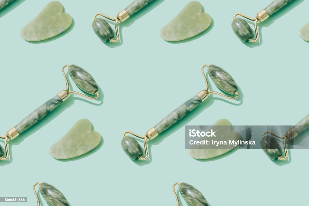 Pattern made with jade gua sha tool and facial roller on pastel green background. Facial massage kit for lifting massage therapy made from natural stones, personal skin care anti-aging tools Pattern made with jade gua sha tool and facial roller on pastel green background. Facial massage kit for lifting massage therapy made from natural stones. Personal skin care anti-aging tools Jade Roller Stock Photo