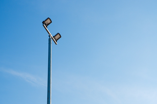 Modern park LED luminaire on a tall metal mast against a blue light sky.
