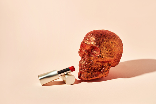Orange skull covered with sequins and red lipstick on a beige background with copy space