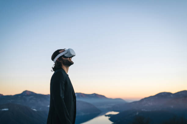 Businessman wears VR glasses on mountain ridge stock photo