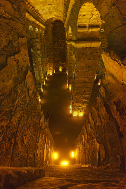 Ancient stone tunnel displaying sarcophagi, lit by warm underground lighting
