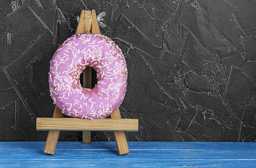 Pink donut decorated with splashes on a dark background.