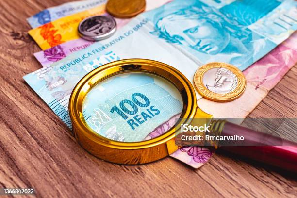 Brazilian Real Banknotes With A Magnifying Glass On Them And Some Coins That Are On Top Of A Wooden Furniture Time Of Financial Crisis With High Inflation Stock Photo - Download Image Now