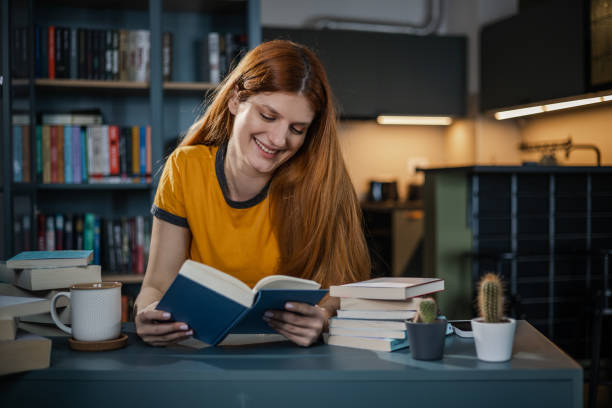 istock Young woman reading a book at home 1366844499