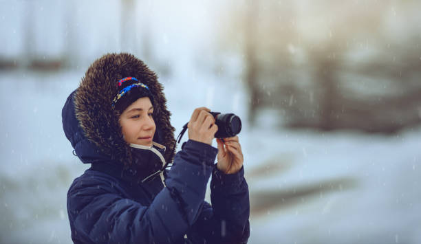 Portrait of a Pretty Woman Making Photo During Snowfall of a Winter Landscape. Photography Hobby. Cold Weather. Happy Active Lifestyle.