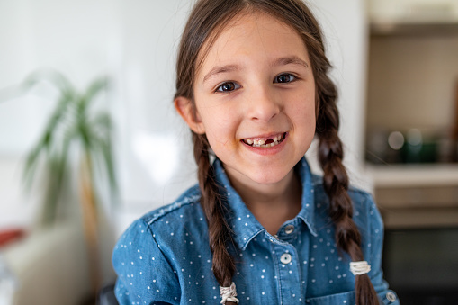 Portrait of a happy cute girl with pigtails smiling without milk tooth at home, she's looking at camera