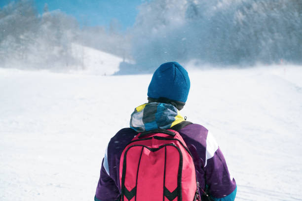 молодой человек в лыжной одежде смотрит на вершину горы. лыжник катается на лыжах в снежную бурю. человек-искатель приключений поднимается  - climbing individual sports sports and fitness snowboard стоковые фото и изображения