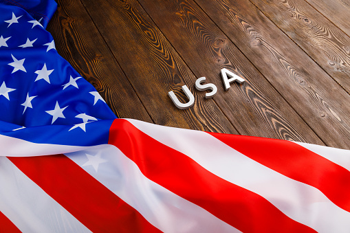 the word USA laid with silver metal letters on wooden board surface with crumpled flag of United States of America in diagonal slanted perspective